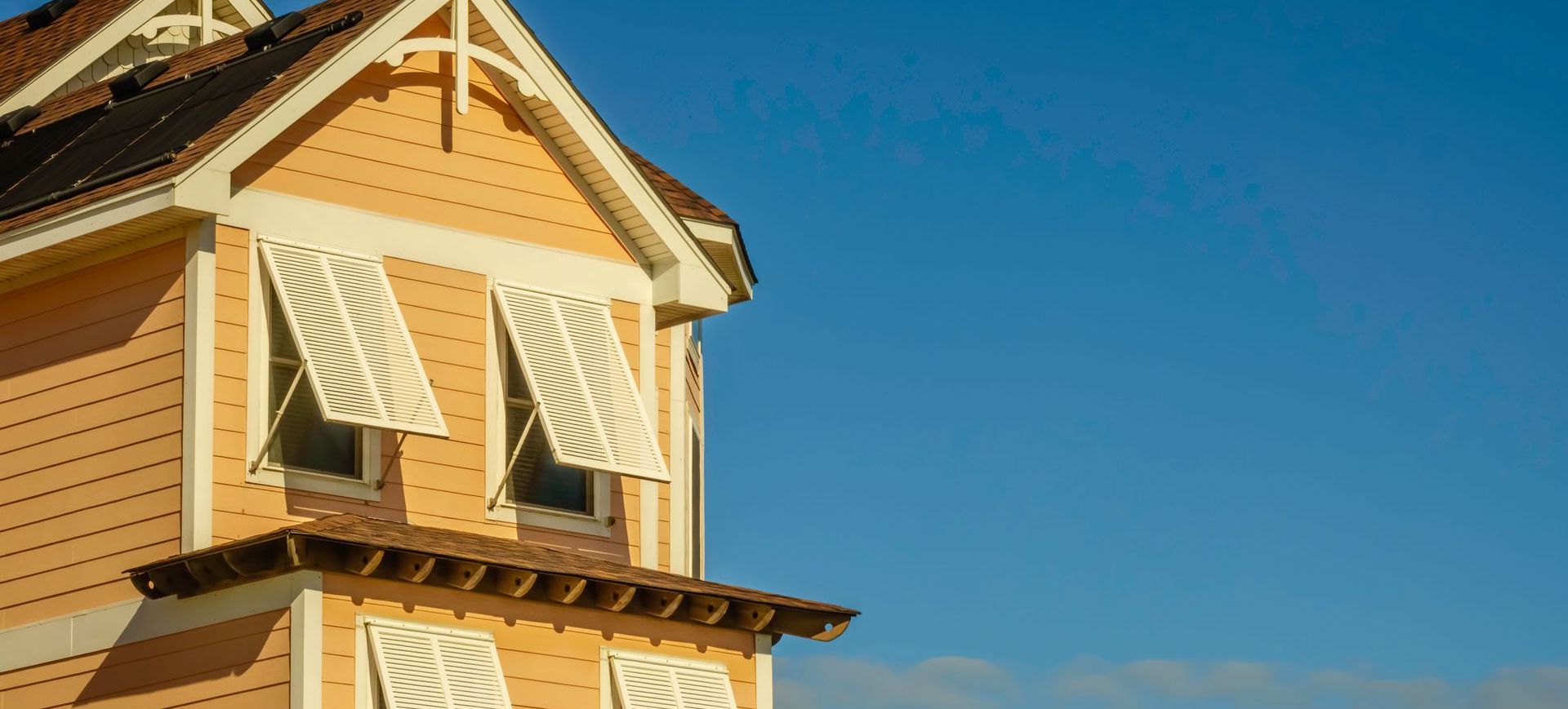 A pale orange house with white trim and open shutters stands against a clear blue sky.