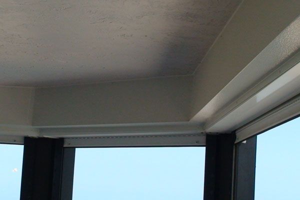 Corner of a room with white ceiling and frame, a window with a blue sky visible.