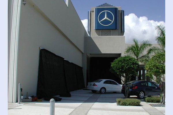 Mercedes-Benz dealership exterior. White and black cars parked outside an entrance beneath the blue logo.