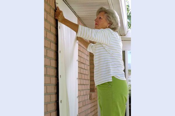 Woman attaching a white storm shutter to a brick wall.