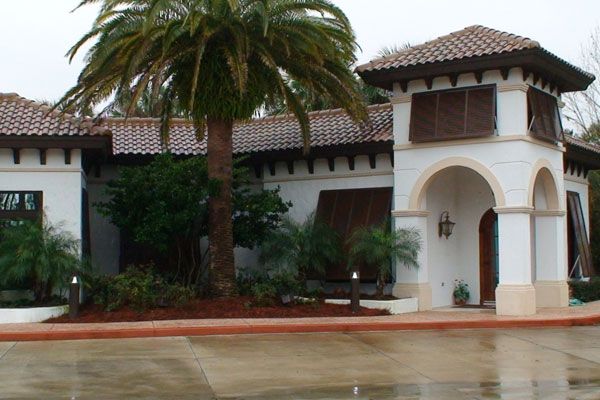 White stucco building with a red tile roof, palm tree, and arched entryway.