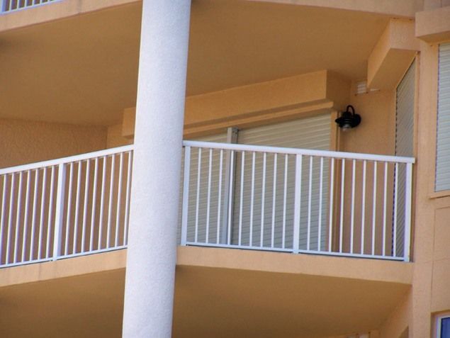 Balcony with white railings and vertical bars, tan building exterior.