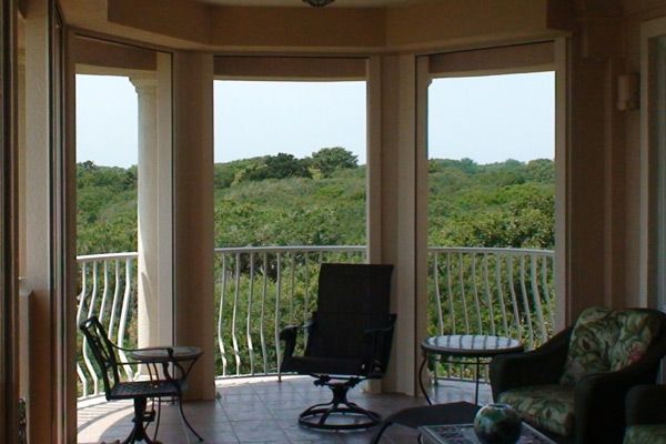 Balcony with view of lush green trees, black chair, white railing, and tiled floor.