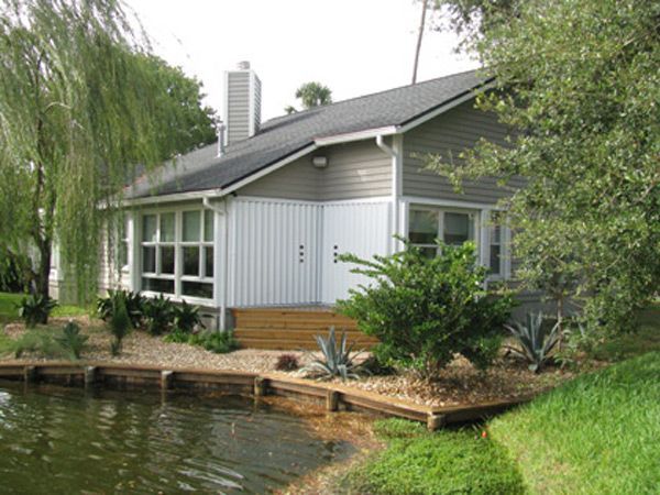 A house with gray and white siding and a dark roof, next to a pond.