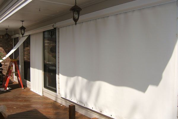 White canvas porch curtains installed on a wooden porch, partially covering windows.