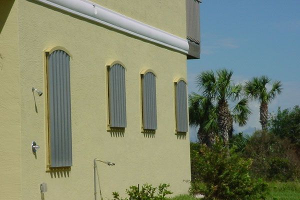 Yellow building with gray storm shutters on windows; palm trees in the background.
