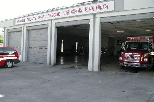 Fire station with three bays. Orange County Fire/Rescue Station 42, Pine Hills sign. A red truck and a red van are parked.