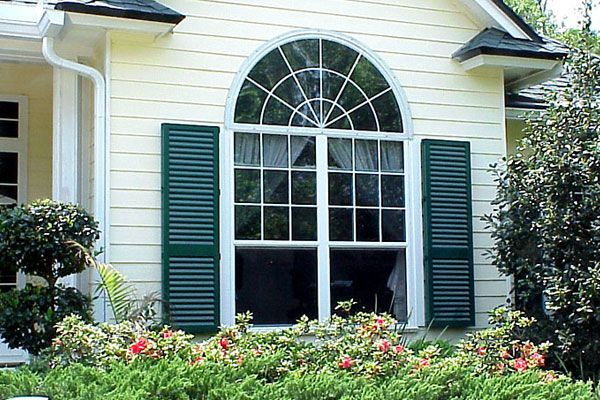 Large arched window with green shutters on a yellow house.