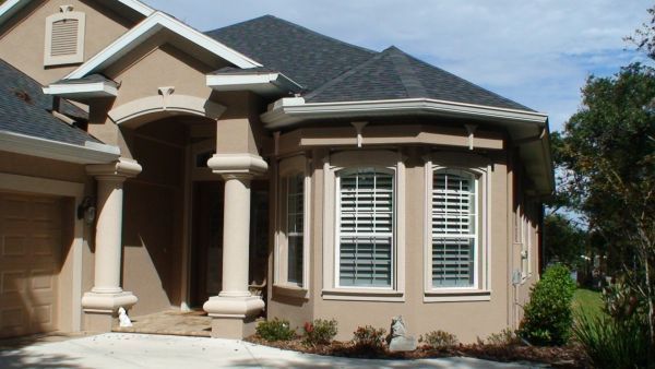 Tan stucco house with white trim, columns, and bay window.