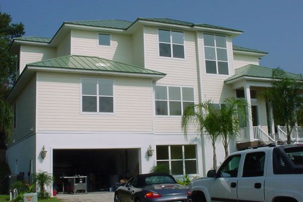 Two-story house with white siding and green roof, open garage with car, white truck, blue sky.