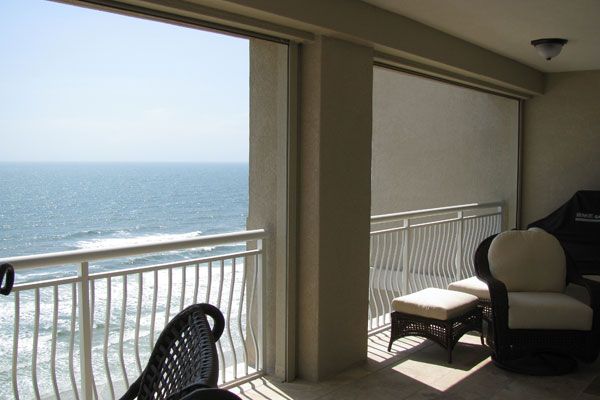 Balcony overlooking ocean; white railing, furniture, and partial shade.