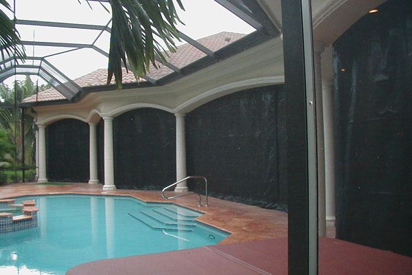Poolside view with black shades, white columns, and blue water.