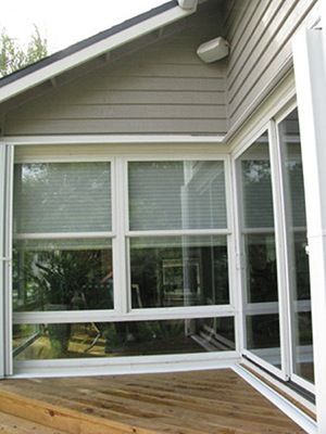 Corner of a building with sliding glass doors and windows, white trim, and a wooden deck.