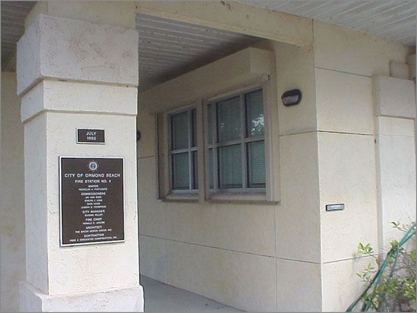Exterior view of a beige building with a sign and two windows.