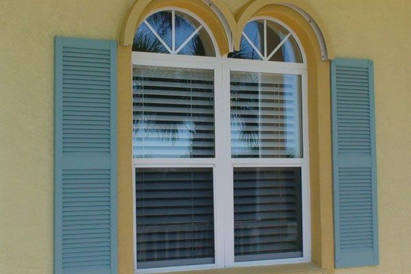 Window with arched top and blue shutters on yellow building.