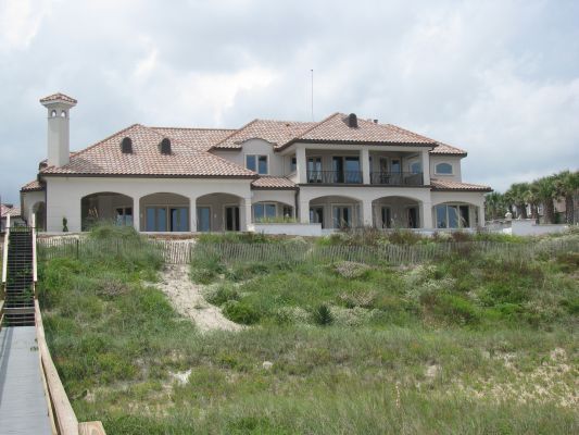 Large beige house with a terracotta roof, overlooking a grassy dune and the ocean.