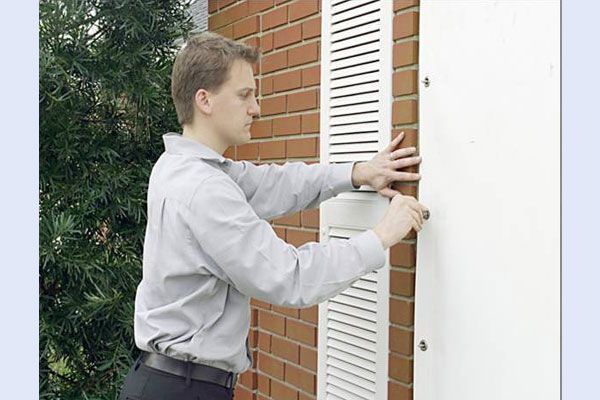 Man attaching a white shutter to a brick house.