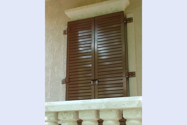 Brown, closed, slatted shutters on a light-colored building, with visible hinges and a stone ledge.