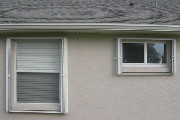 Two windows on a light beige house wall, one with blinds partially covering it, other with clear glass.