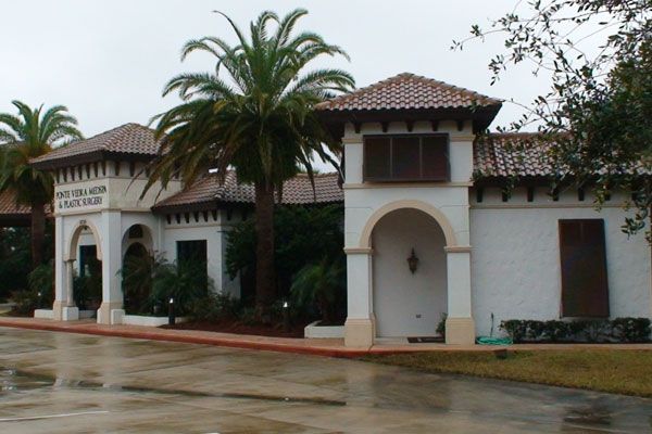 Spanish-style building with white walls, red-tiled roof, arches, and palm trees.