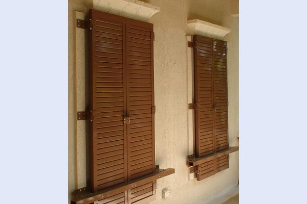 Two brown wooden shutters on a light-colored building, each with a small window box.