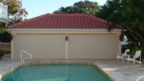 Pool in foreground, light tan garage with red tile roof. White chairs to the right.