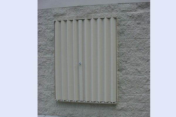 Beige corrugated hurricane shutter on a gray brick wall.
