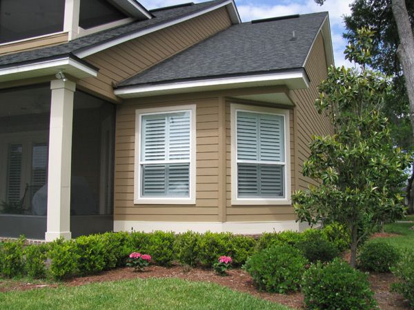 Tan house exterior with shuttered windows, dark roof, and landscaping.