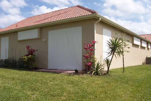 Beige house with orange roof, white shutters, and green grass and plants.
