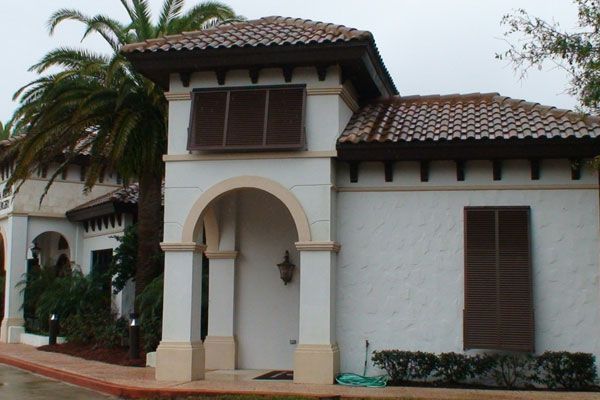 White stucco building with brown shutters and tile roof, archway entrance.