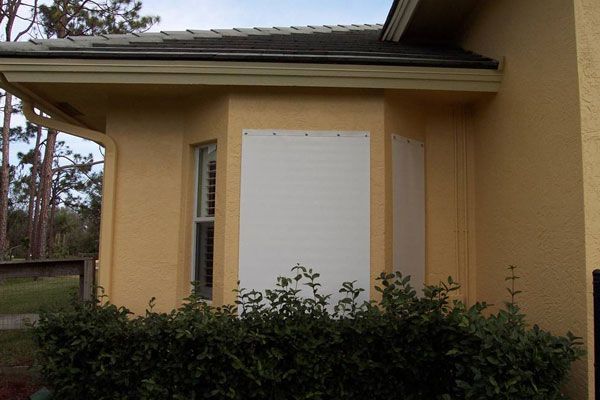 Exterior of a building with boarded-up bay windows, yellow stucco walls, and a dark roof.
