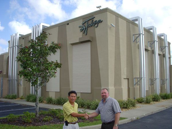 Two men shaking hands in front of a beige building with a 