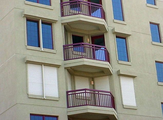 Building exterior with balconies. Tan walls, windows, and burgundy railings.