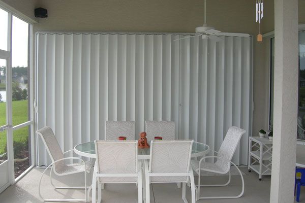 Patio with closed white accordion hurricane shutters, round table, chairs.