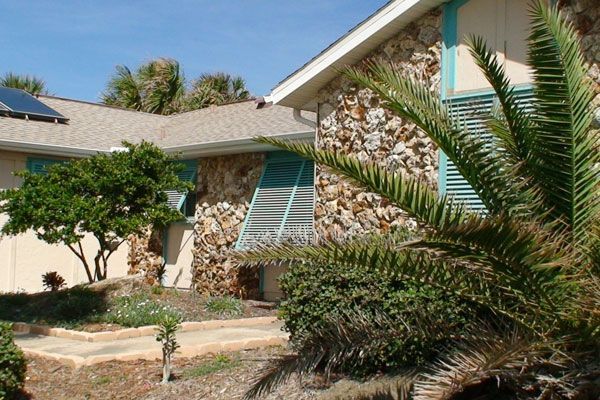 Building exterior with textured stone facade, turquoise shutters, palm tree, and solar panels on the roof.