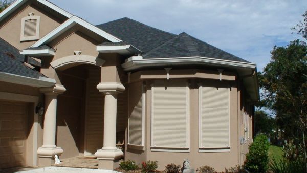 Tan house with cream columns and shutters; dark roof.