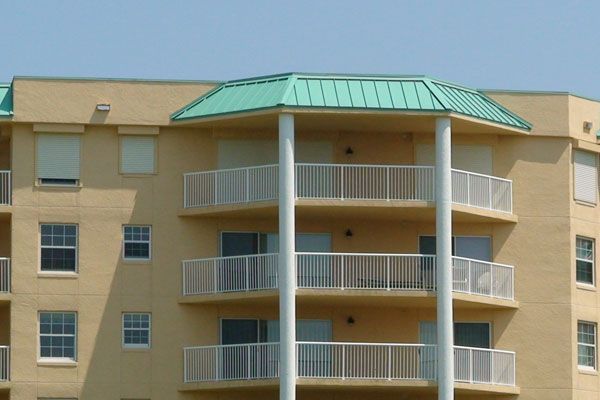 Tan multi-story building with green roof, white balconies.