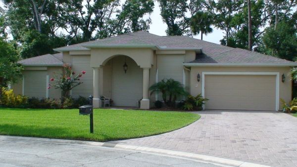 Tan stucco house with a dark roof and a curving driveway on a green lawn.