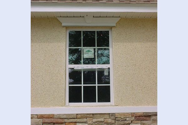 Window with white frame, paneled glass, and decorative trim on stucco exterior.
