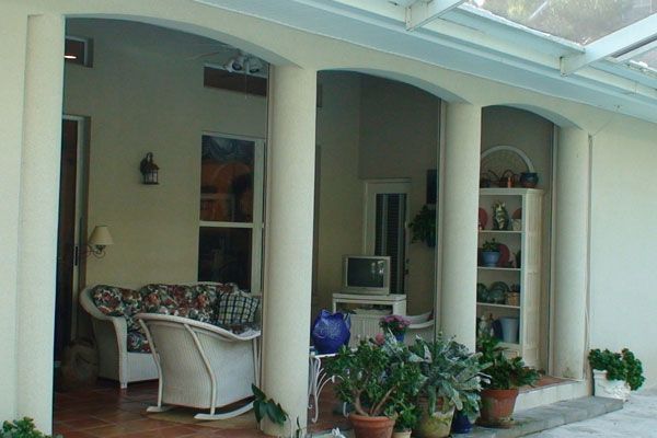 Covered patio with columns, couches, television, and plants in pots.
