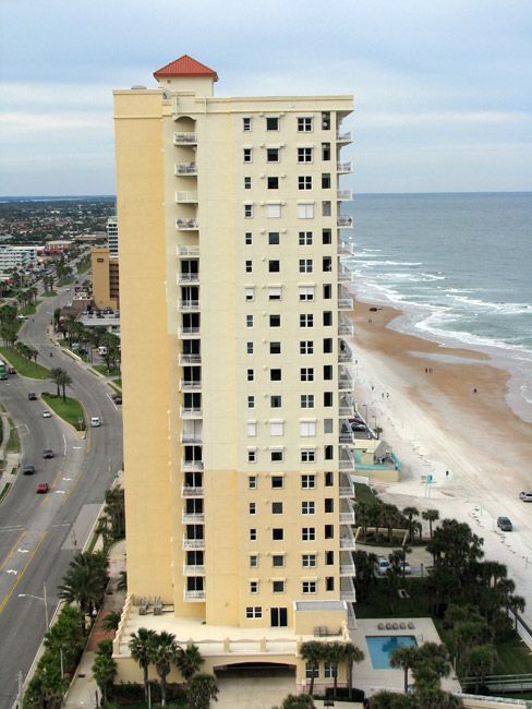 Tall beige beachfront condominium building with ocean and beach view.
