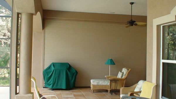 Covered grill, patio furniture, and closed tan security shutter on a covered patio.