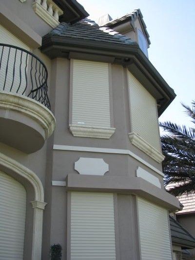 Tan house with shuttered windows. Black iron balcony railing.