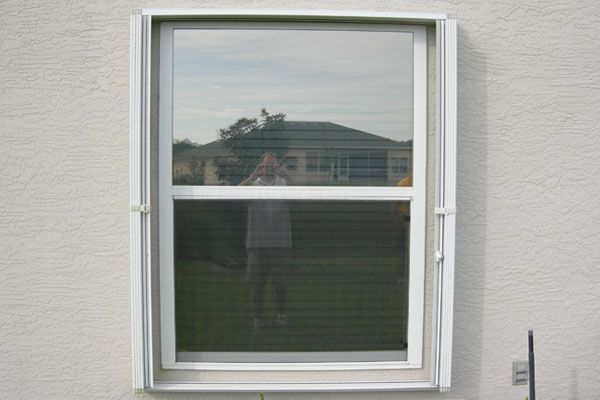White framed window with a screen; reflecting a person taking photo outside of a white stucco building.