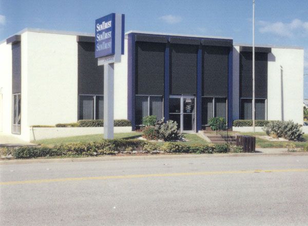 SunCoast bank building with a sign on a sunny day. White walls, black window shades and blue trim.