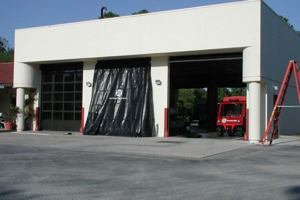 Fire station with two open bays, one covered by black fabric. Red fire truck inside.