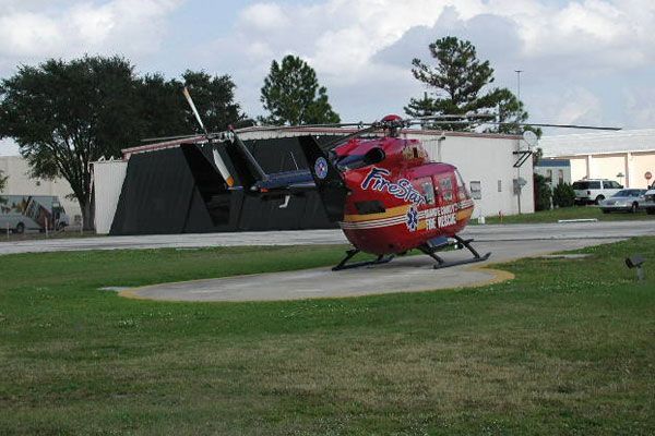 Red air ambulance helicopter on a landing pad near a building.