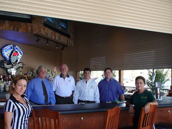Bar staff posing behind a bar; interior setting.