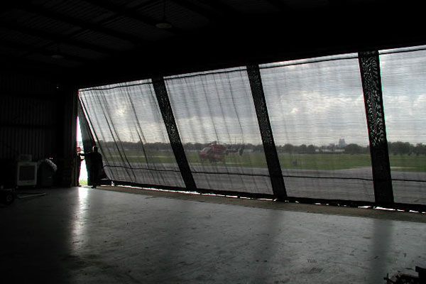 Open hangar with a large, partially open door revealing a grassy field and distant buildings.