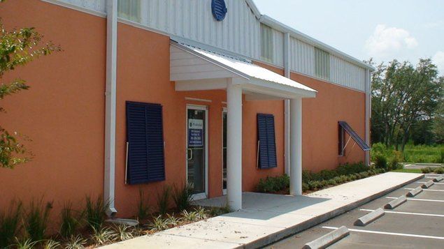 Orange building with white awning over doorway, blue shutters, and sidewalk.